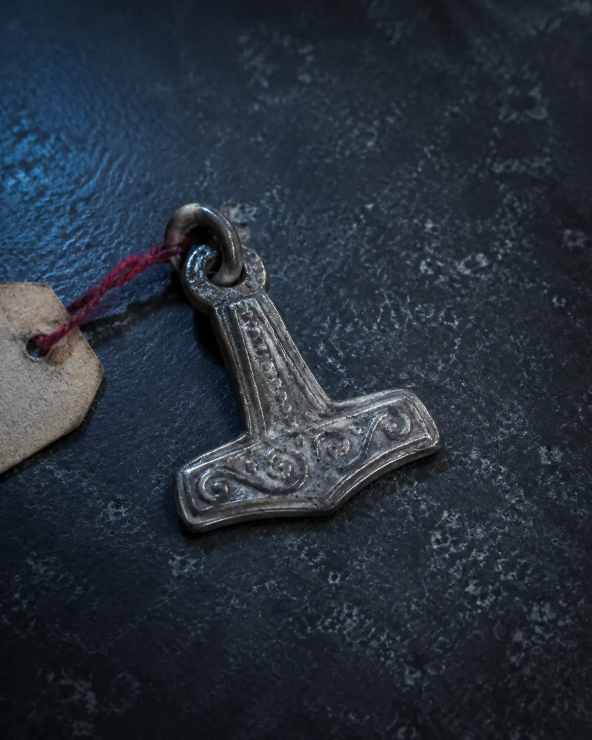 A historically inspired silver Thor's hammer pendant on a dark conservation table